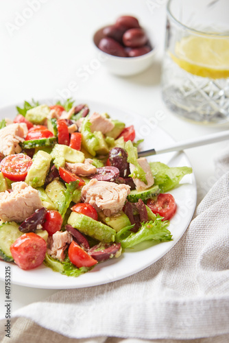 Salad with tuna, lettuce, cucumbers, tomatoes, olives and avocados in white plate on the table