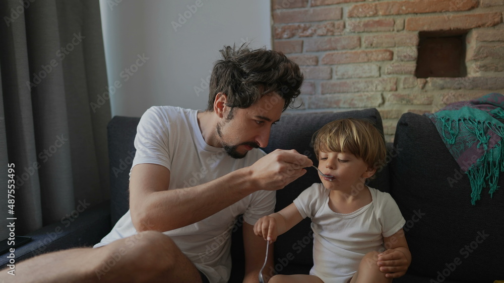 Fototapeta premium Candid family moment father feeds toddler child yogurt breakfast in morning