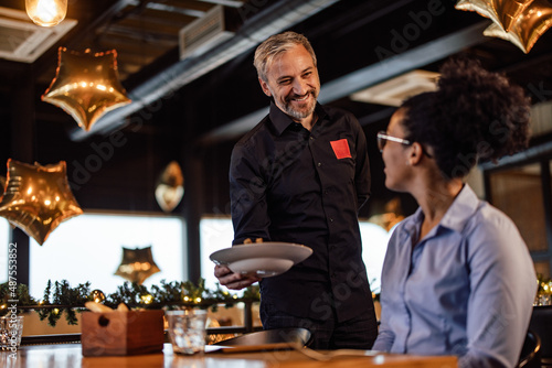 Friendly caucasian waiter  brinking a meal to his african-american female customer.