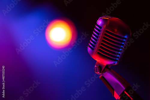 Classic stage microphone. Object illuminated with colored light. In the background, a view of blurred lights on the stage.