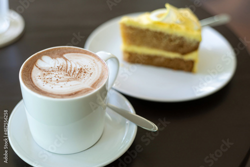cup of hot coffee art with cake on wooden table in cafe
