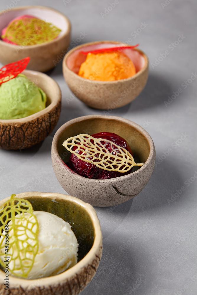 Assorted ice cream balls in ceramic dishes. Frozen dessert - ice cream with vanilla, pistachio, mango, blueberry and strawberry flavours on gray stone background. Minimalistic composition gelato. Assorted ice cream balls in ceramic dishes. Frozen dessert - ice cream with vanilla, pistachio, mango, blueberry and strawberry flavours on gray stone background. Minimalistic composition gelato.