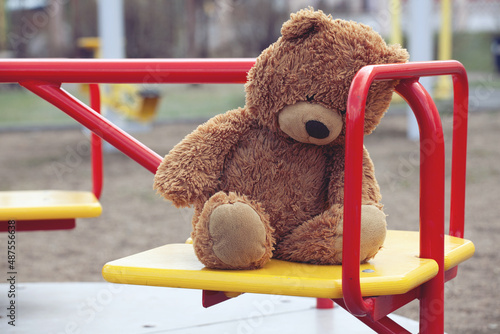 Forgotten Brown Teddy Bear on a Childrens Carousel in an Empty Playground. Concept Childhood, Psychology, Relationships, Growing up, Orphanage, Kindergarten, Foster Home