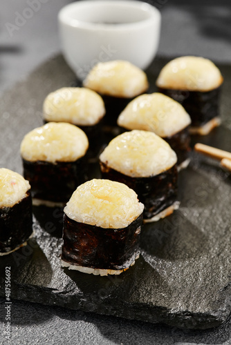 Baked Maki sushi on dark slate. Hot cheese hosomaki roll. Simple sushi roll with cheese, baked cheese topped. Style concept japanese menu with black background, leaves and hard shadow.