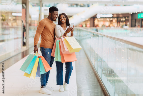 Portrait of excited black couple using phone in shopping mall