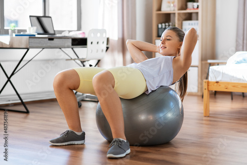 sport, fitness and healthy lifestyle concept - smiling teenage girl exercising with exercise ball at home