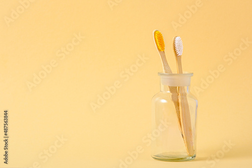 two bamboo toothbrushes in glass cup on beige background  eco natural products for oral hygiene