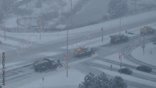 High angle shot of five snow ploughing trucks driving up the highway and clearing the snow off the road through heavy snowfall. photo