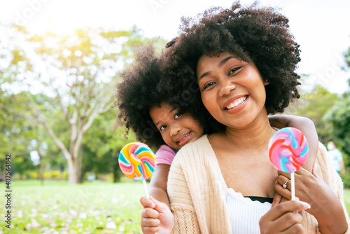 Beautiful mom and her daughter holding Multi-Colored Rainbow Hard Lollipop Candy while picnic at the park. Concept of relaxing and special holiday