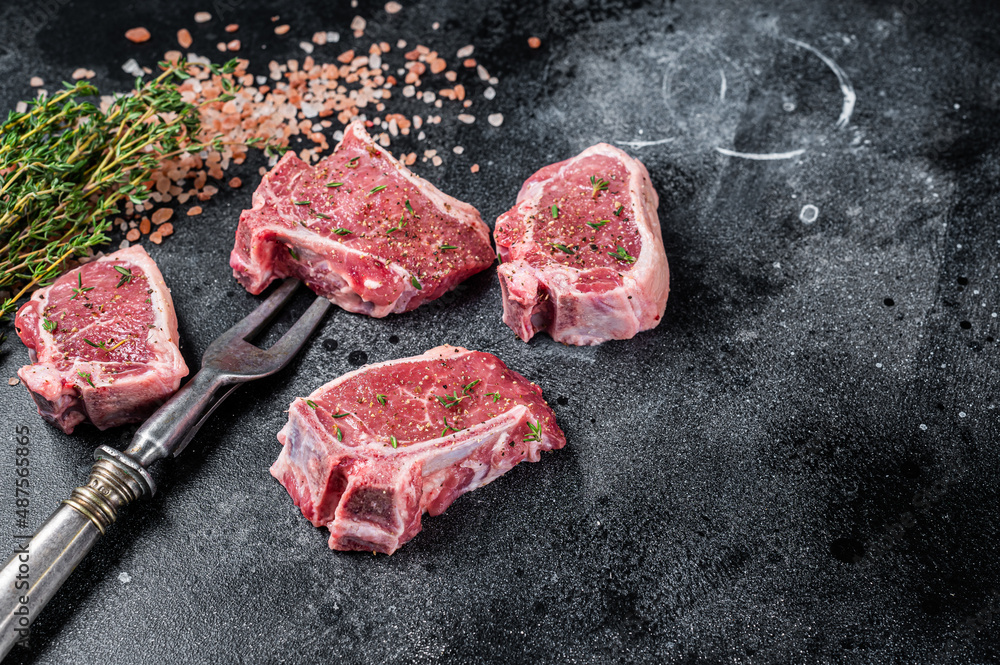 Raw lamb loin steaks, chops cutlets on kitchen table. Black background. Top view. Copy space