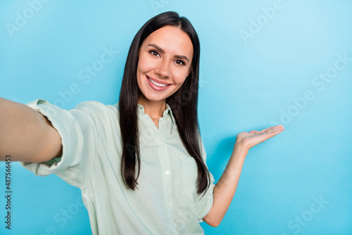 Photo of young pretty woman indicate hand empty space invite make selfie isolated over blue color background