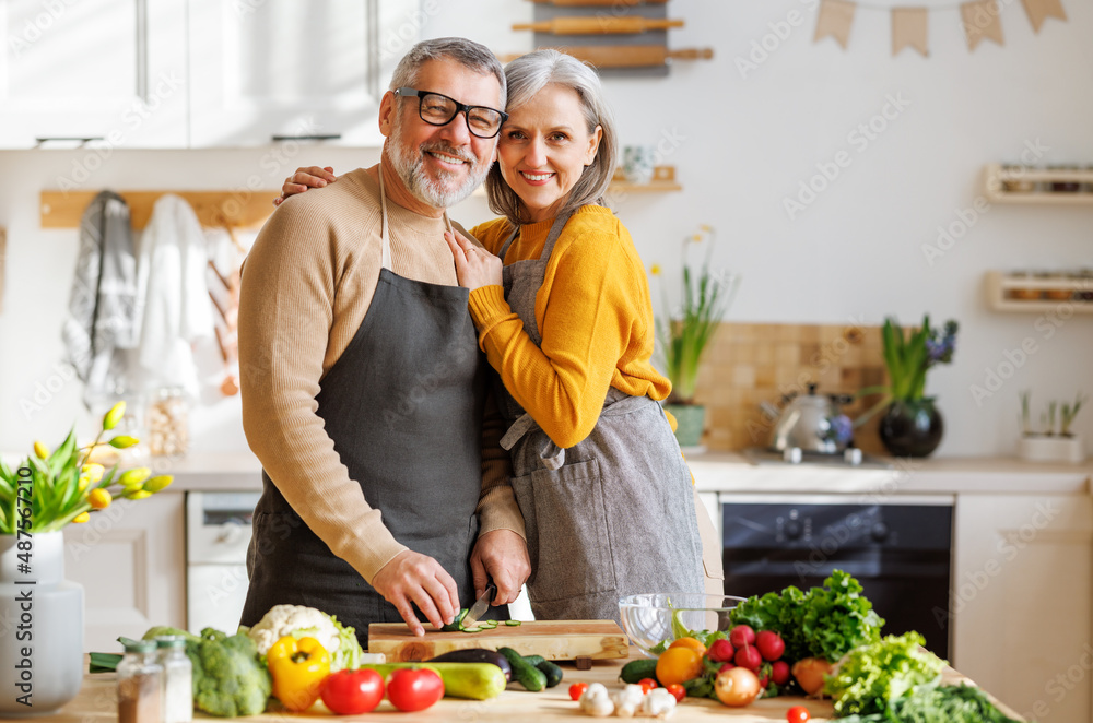 Happy elderly family couple wife and husband embracing while cooking vegetarian food together Happy elderly family couple wife and husband embracing while cooking vegetarian food together