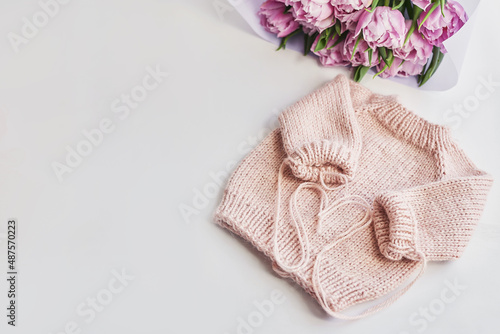 Knitted kids clothes and accessories for knitting. Needlework and knitting. Hobbies and creativity. Knit for children. Handmade. Pink sweater and tulips