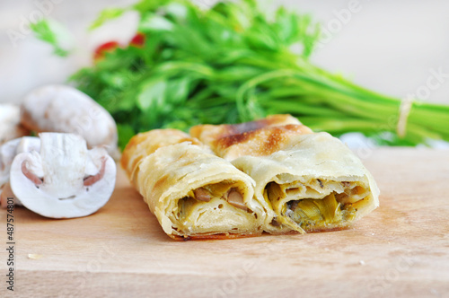Homemade mushrooms pie.Fresh piece of savory strudel stuffed with  leek and mushrooms served on a wooden plate,with mushrooms and parsley