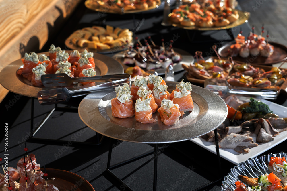 Salmon rolls stuffed with dill cheese. A silvery dish, luxury catering, a richly laid table.
