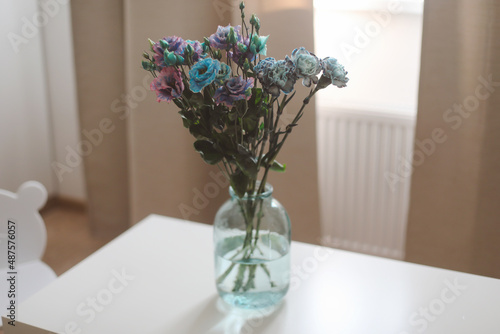 bunch of blue and purple flowers in a jar on the table in a sunny room, minimal home decor