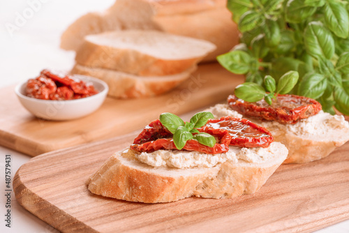 Classic italian appetizer - bruschettas or toasts with ricotta cheese and sliced sun dried tomatoes topped with basil on wooden table background. Delicious appetizer