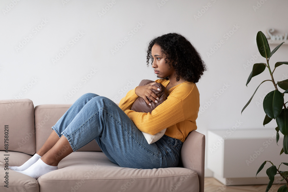 Unhappy young black woman suffering from depression, hugging pillow, sitting on couch at home Unhappy young black woman suffering from depression, hugging pillow, sitting on couch at home