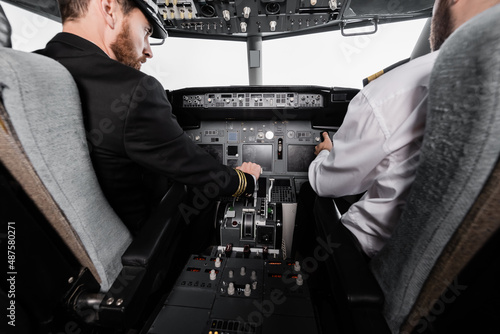 bearded pilot in cap using thrust lever near co-pilot in airplane simulator. © LIGHTFIELD STUDIOS
