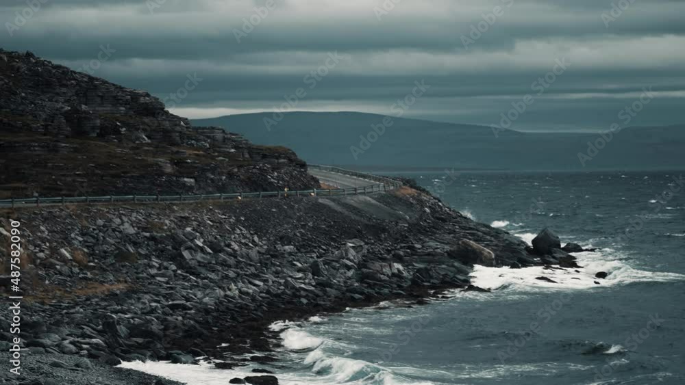 The narrow road winds along the coastline. Powerful waves hit the shore. Heavy clouds cover the sky. Slow-motion, pan left. The narrow road winds along the coastline. Powerful waves hit the shore. Heavy clouds cover the sky. Slow-motion, pan left.