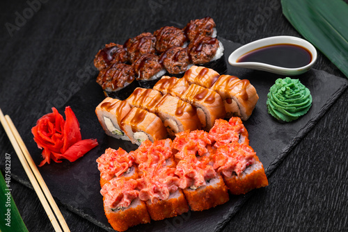 sushi rolls laid out on a dark background decorated with bamboo leaves and chopsticks