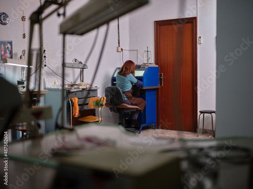 an unrecognizable adult woman working sitting in a polishing machine with a safety box in her jewelry workshop