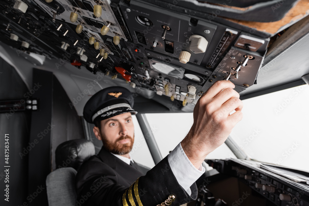 pilot in cap and uniform reaching overhead panel in airplane simulator. pilot in cap and uniform reaching overhead panel in airplane simulator.