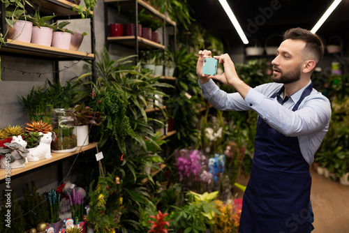 a garden center worker takes a picture of a display case with potted plants on his phone