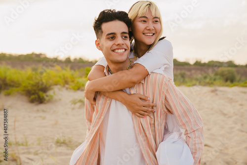 Multiracial young couple smiling while piggybacking on summer beach