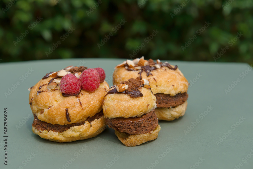 Muffins of small sizes with raspberries on a green background in bright sunlight in the garden. Summer mood.Confectionery blog,banner in a cafe and a restaurant. Menu of confectionery.A tempting offer