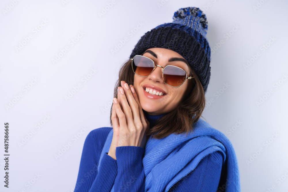 Young woman in a blue golf turtleneck, hat and scarf, sunglasses, on a white background, cheerful in a good mood Young woman in a blue golf turtleneck, hat and scarf, sunglasses, on a white background, cheerful in a good mood
