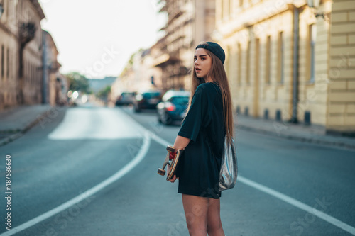Young woman holding her skateboard and standing on the road in the city