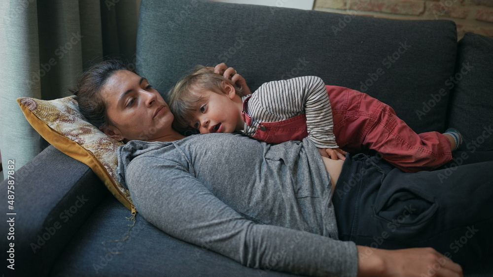 Obraz premium Exhausted mother lying on sofa with child