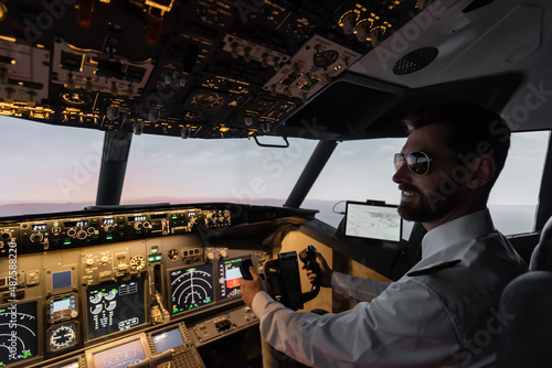 cheerful pilot in sunglasses using yoke while piloting in evening.