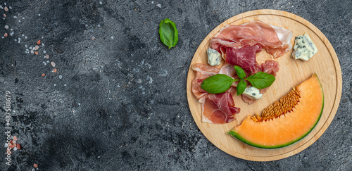 Antipasti. Fresh melon with prosciutto and basil on dark stone table. Italian food. Long banner format. top view