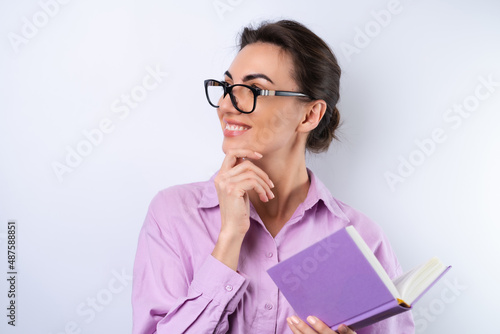 A young woman in a lilac shirt on a white background holds a book in her hands in glasses for vision