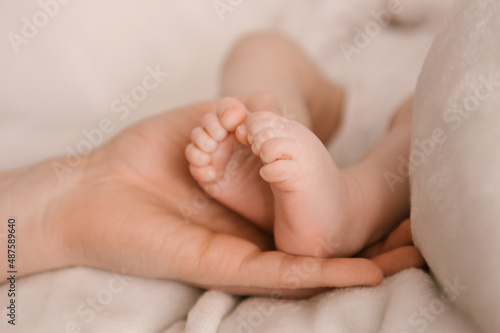Small legs of a newborn girl in the hand of the pope on a light background