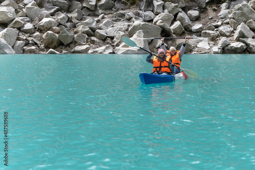 Two friends paddling a kayak in a turquoise water lake in the mountains.