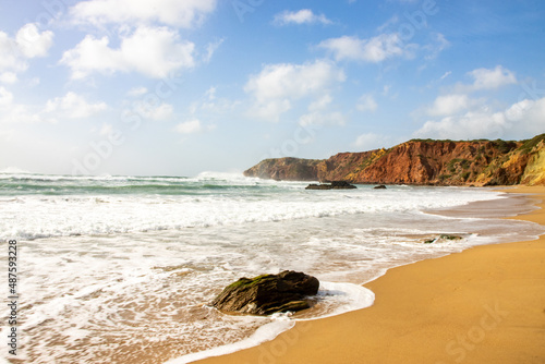 Beach with golden sand, clear water, blue sky and red cliffs in Algarve, Portugal
