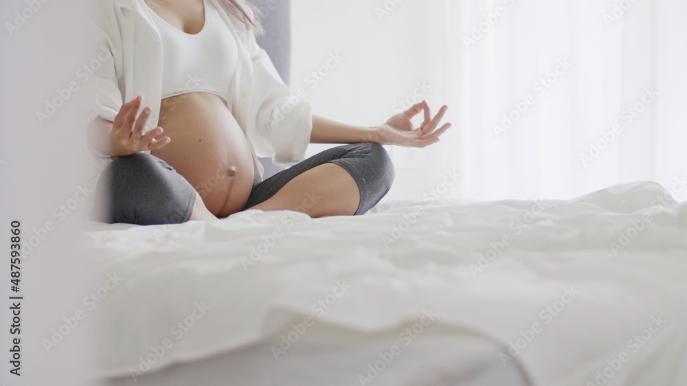 Beautiful Asian healthy pregnant woman practicing yoga in the bedroom at home.