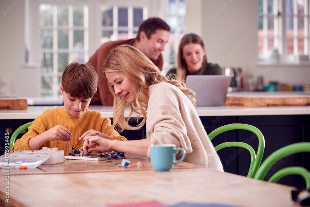 Mother Helps Son With Electronics Project Sitting At Kitchen Table At Home With Laptop Mother Helps Son With Electronics Project Sitting At Kitchen Table At Home With Laptop