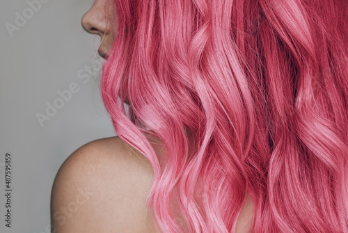 Close-up of the wavy pink hair of a young woman isolated on a gray background. Result of coloring, highlighting, perming. Beauty and fashion photo