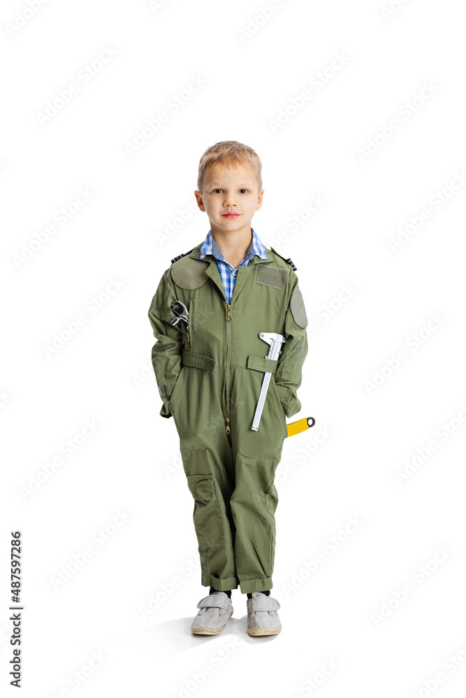 Portrait of little boy, cute kid in image of auto mechanic or fitter in green dungarees with work tools isolated over white studio background. Childhood, education concept Portrait of little boy, cute kid in image of auto mechanic or fitter in green dungarees with work tools isolated over white studio background. Childhood, education concept