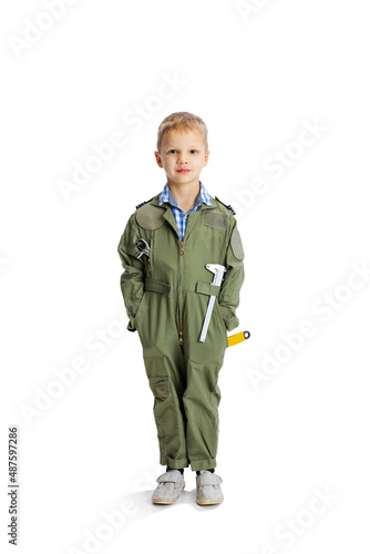 Portrait of little boy, cute kid in image of auto mechanic or fitter in green dungarees with work tools isolated over white studio background. Childhood, education concept