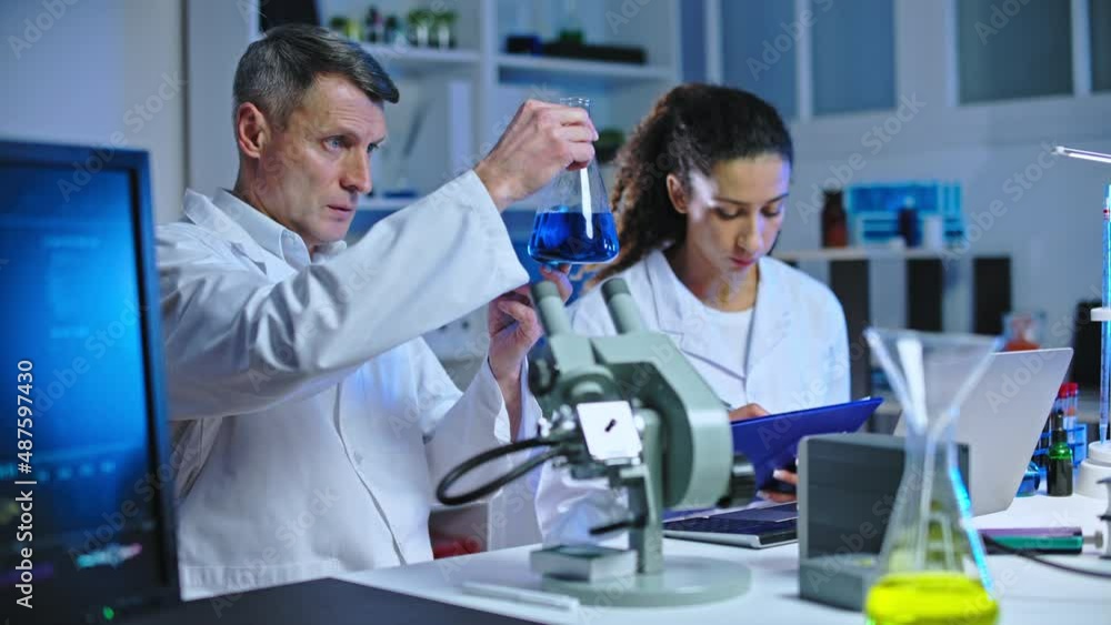 Two scientists examining chemical reaction in glass flask, making lab research Two scientists examining chemical reaction in glass flask, making lab research