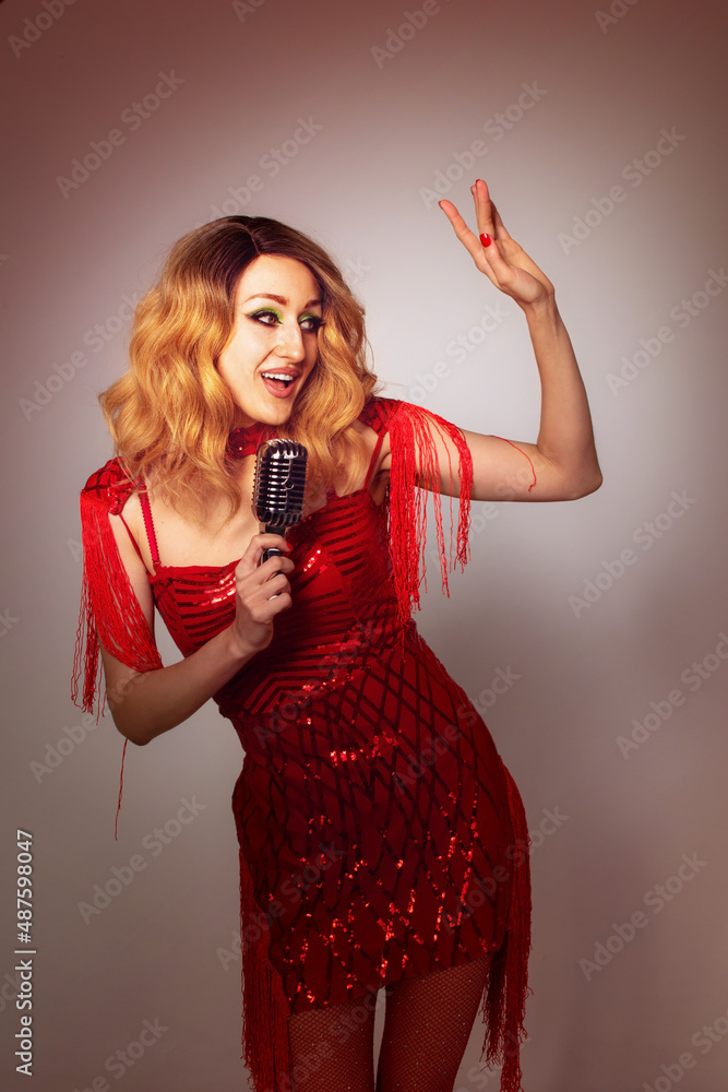 Beautiful young female singer wearing vivid makeup and fancy red dress holding a silver microphone singing, on gray background Beautiful young female singer wearing vivid makeup and fancy red dress holding a silver microphone singing, on gray background