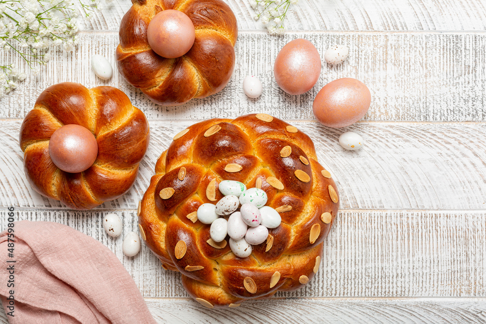 Fototapeta premium Easter background with italian style braid bread and pink metallic colored eggs. Homemade pastry. White flowers. White wooden background. Top view.