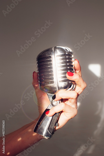Vintage silver microphone; woman holding a mic in hand, with lens flare; isolated on gray background