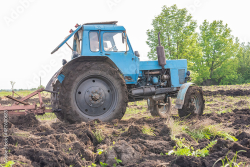 Old blue tractor on the field working. Farmer plowing stubble field in tractor preparing plows the land, agricultural works at farmlands, agriculture tractor-landscape. Tractor Plowing.