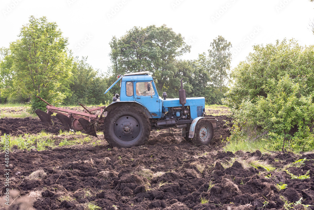 Old blue tractor on the field working. Farmer plowing stubble field in tractor preparing plows the land, agricultural works at farmlands, agriculture tractor-landscape. Tractor Plowing. Old blue tractor on the field working. Farmer plowing stubble field in tractor preparing plows the land, agricultural works at farmlands, agriculture tractor-landscape. Tractor Plowing.